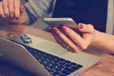 closeup van vrouw die aan laptop zit met smartphone in de hand