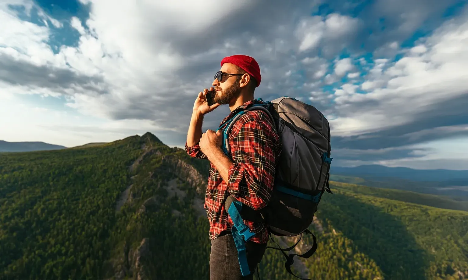 Man kijkt telefonerend voor zich uit, in een mooi berglandschap.