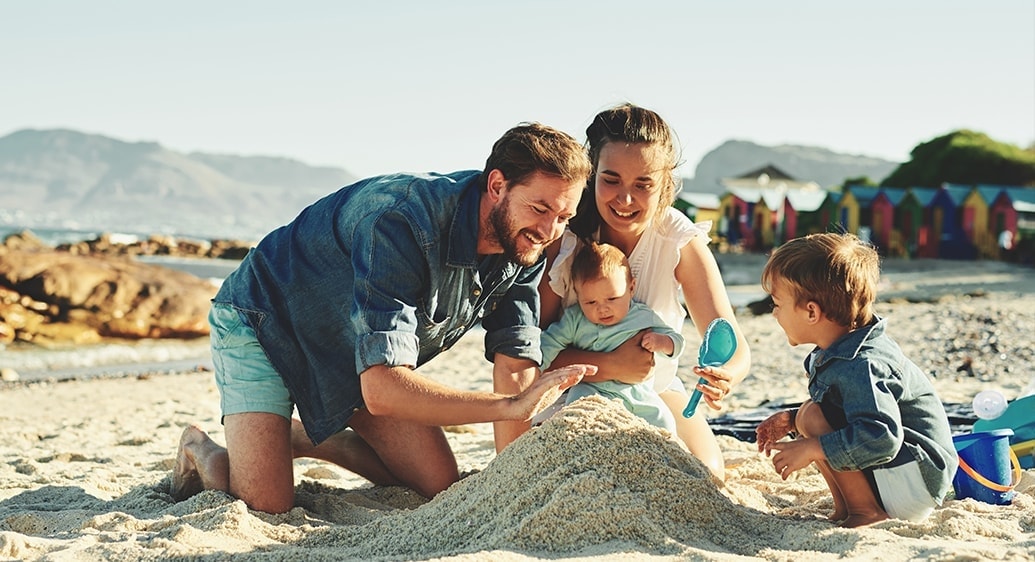 familie van man, vrouw, zoon en baby werken op het strand samen aan een zandkasteel in de zon