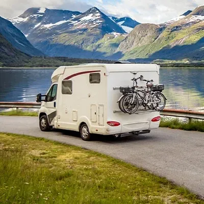 kleine motorhome met fietsen rijdt langs een meer in een bergachtig landschap