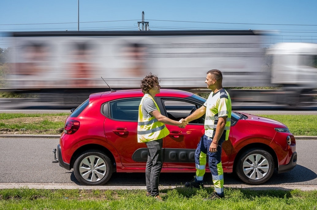 man en VAB-wegenwachter schudden de hand voor een rode auto aan de rand van een drukke weg