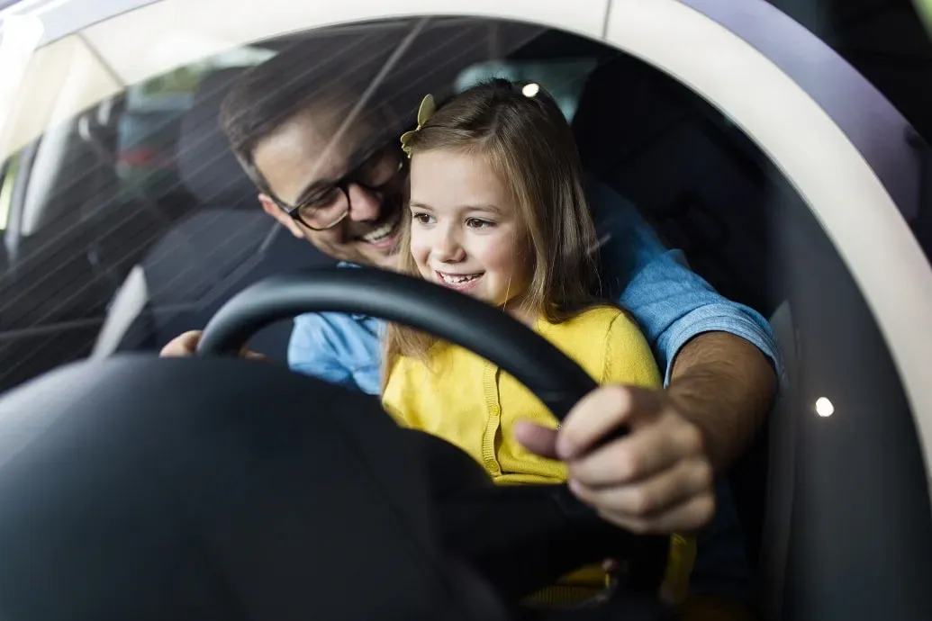 papa en dochter proberen samen een auto uit in de showroom