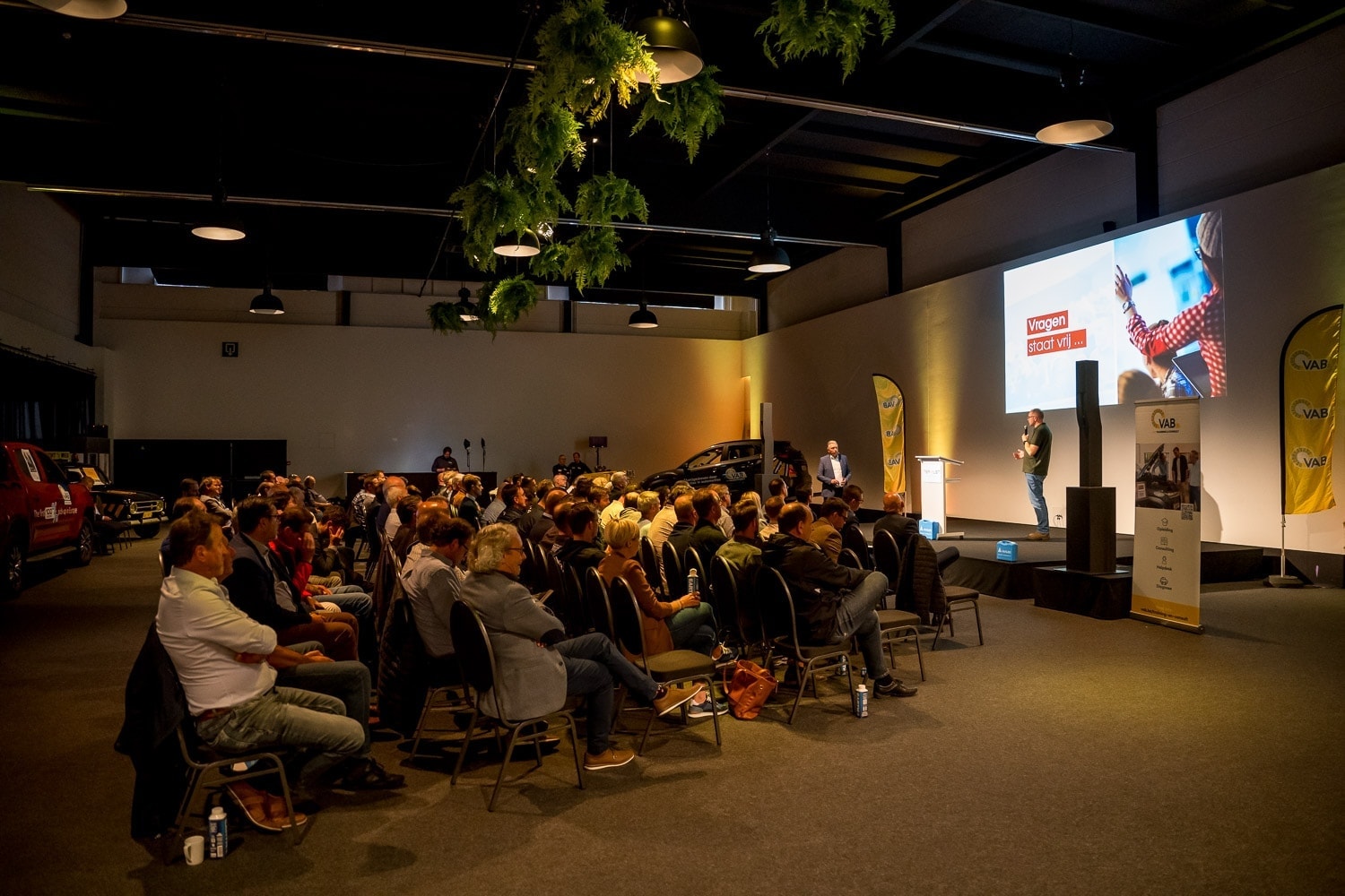 mensen zitten in een zaal te luisteren naar een presentatie over VAB 