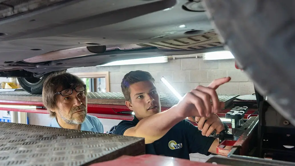 2 mannen kijken een probleem na aan een band van een auto die op een autobrug staat