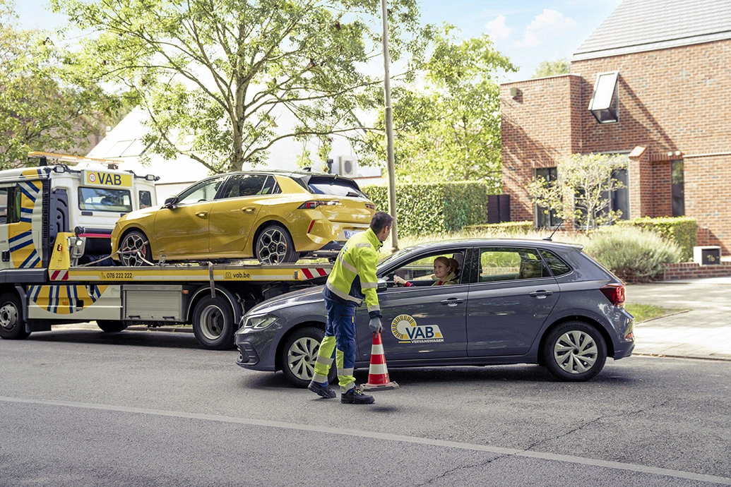 een VAB-wegenwachter zet een kegeltje voor een VAB-vervangwagen en zijn takelwagen, waarop een gele auto staat die weggetakeld moet worden