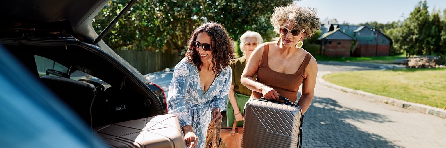 enkele vrouwen laden koffers in een auto in op een zonnige dag