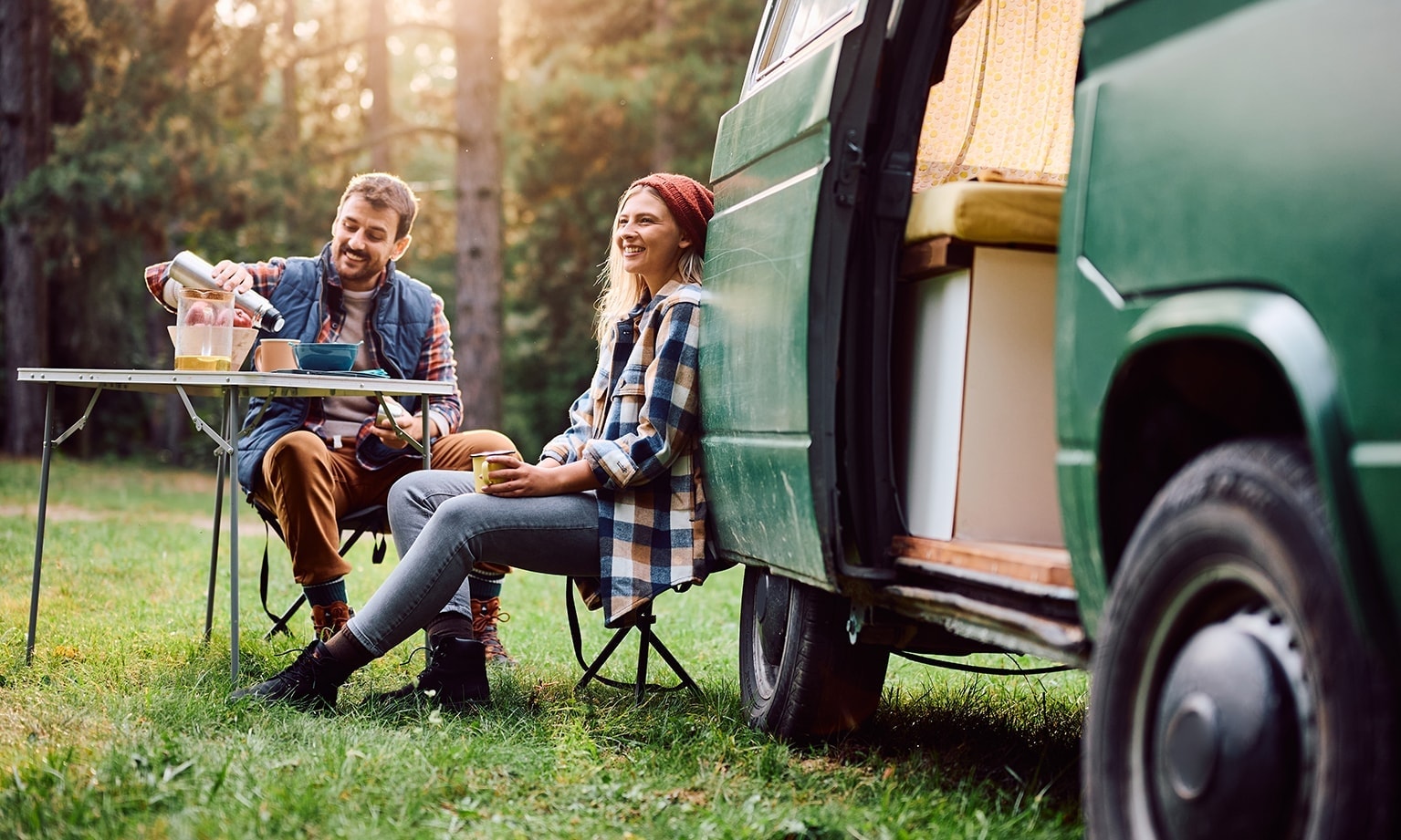 Een man en vrouw genieten samen van het lenteweer in de natuur, naast hun campervan of busje