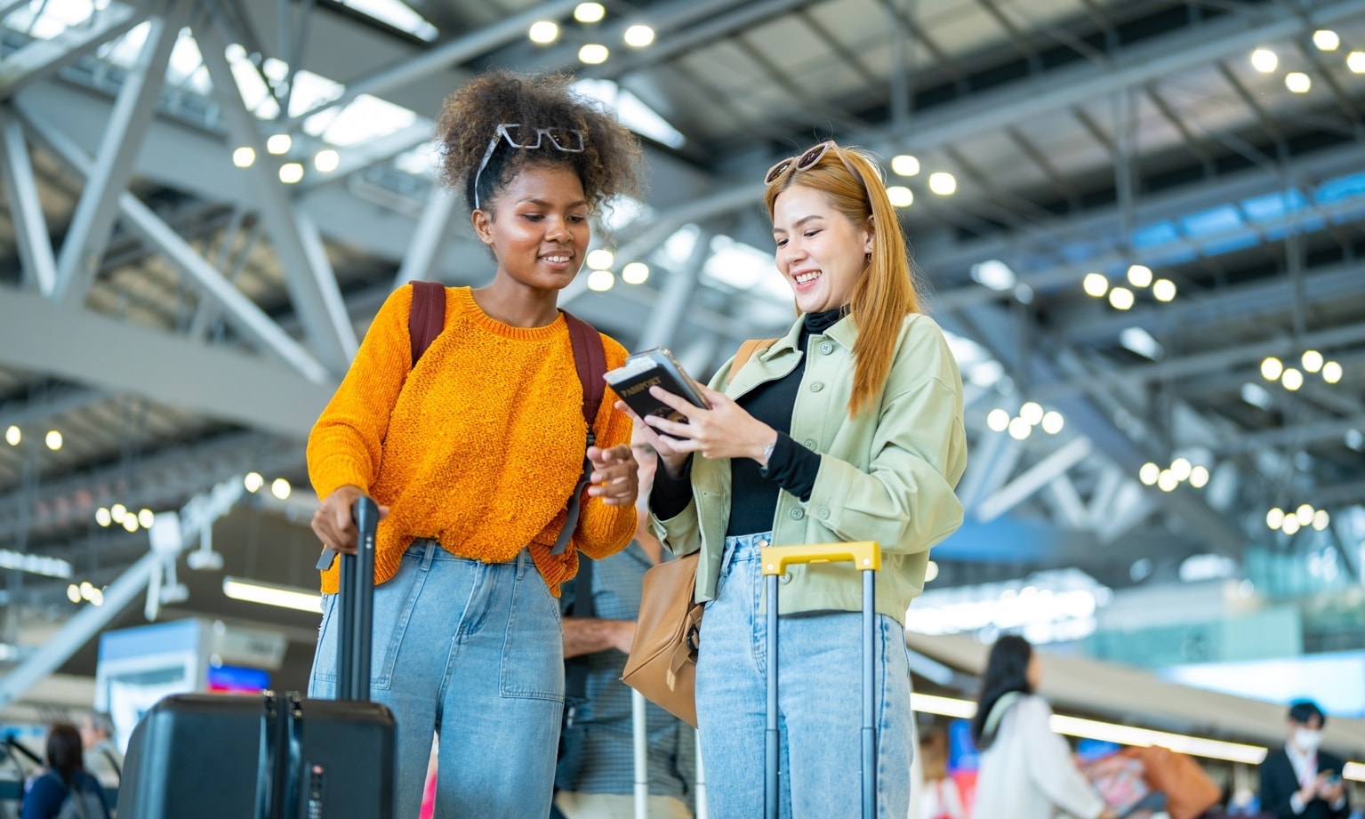 Twee reizigers bekijken samen een smartphone in een moderne luchthaven met bagage.